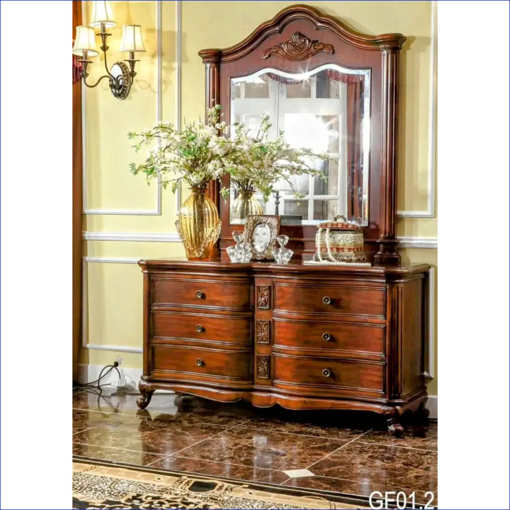 Ornate wooden dresser with mirror and decorative carvings topped with floral arrangement.